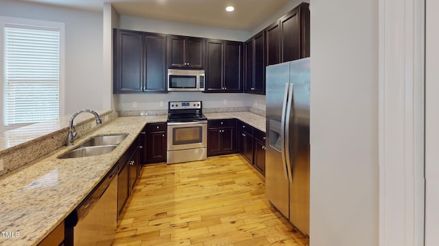 kitchen featuring appliances with stainless steel finishes, light hardwood / wood-style flooring, sink, and light stone countertops