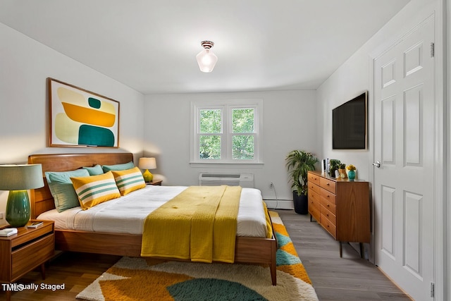 bedroom with a wall mounted air conditioner, hardwood / wood-style floors, and baseboard heating