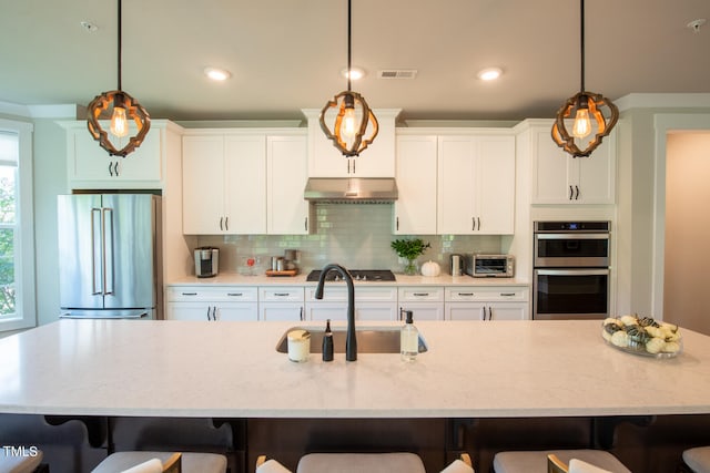 kitchen with appliances with stainless steel finishes, a large island with sink, sink, and pendant lighting