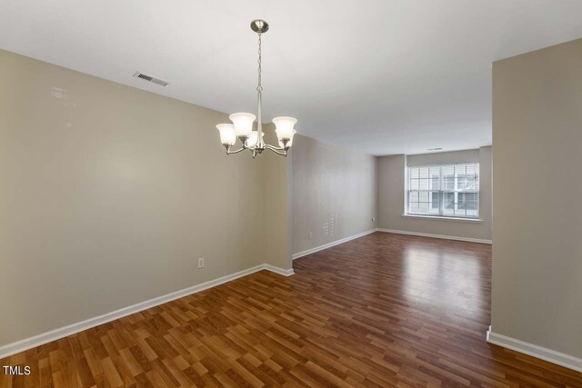 spare room featuring dark hardwood / wood-style flooring and a chandelier