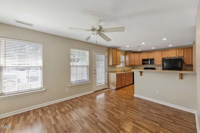 kitchen featuring a breakfast bar, kitchen peninsula, black appliances, ceiling fan, and light hardwood / wood-style flooring