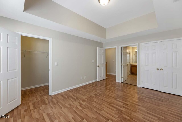 unfurnished bedroom with light wood-type flooring, a tray ceiling, and ensuite bathroom