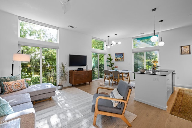 living room with ceiling fan with notable chandelier, a towering ceiling, sink, and light hardwood / wood-style floors