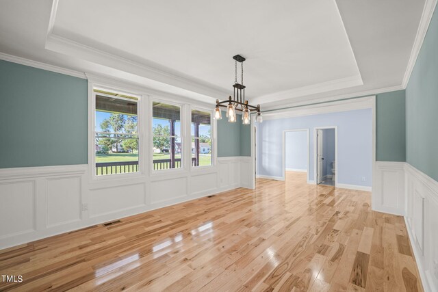 empty room featuring crown molding, light hardwood / wood-style flooring, an inviting chandelier, and a tray ceiling