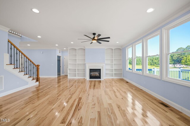 unfurnished living room with crown molding, built in shelves, ceiling fan, and light hardwood / wood-style floors