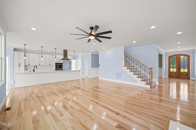 unfurnished living room featuring french doors, light wood-type flooring, sink, ceiling fan, and ornamental molding