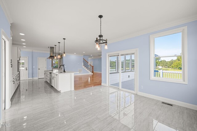 kitchen with white cabinets, crown molding, decorative light fixtures, a chandelier, and a kitchen island with sink