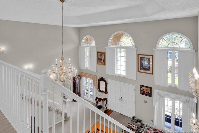 foyer entrance with a textured ceiling, a high ceiling, a notable chandelier, and a tray ceiling