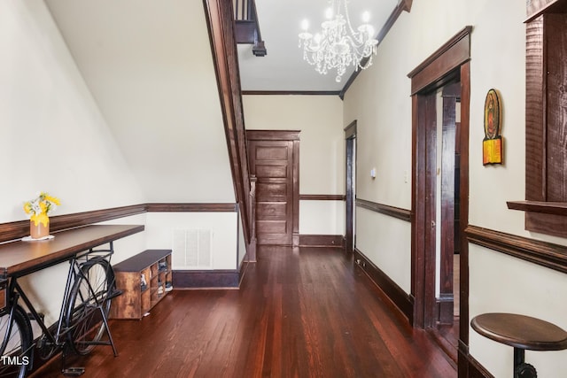 corridor featuring wood finished floors, baseboards, visible vents, ornamental molding, and a notable chandelier