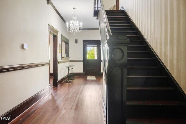 stairway with wood finished floors, baseboards, a chandelier, and ornamental molding