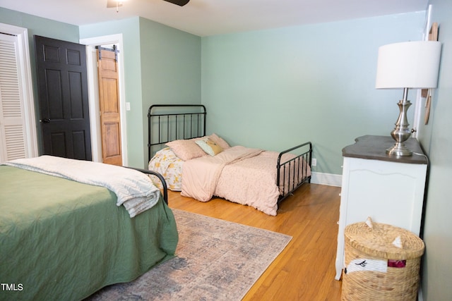 bedroom featuring a barn door, a closet, ceiling fan, and light hardwood / wood-style floors