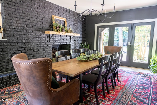 dining room with brick wall, a notable chandelier, french doors, and a fireplace