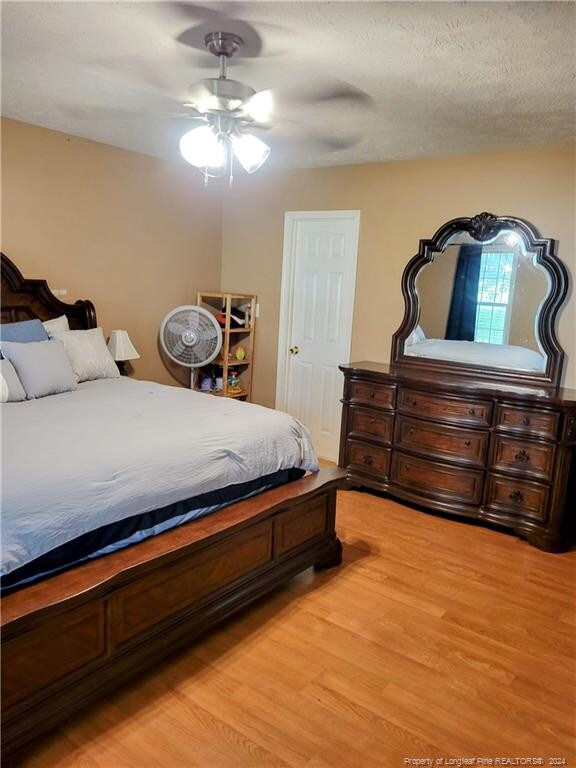 bedroom with a textured ceiling, light hardwood / wood-style flooring, and ceiling fan