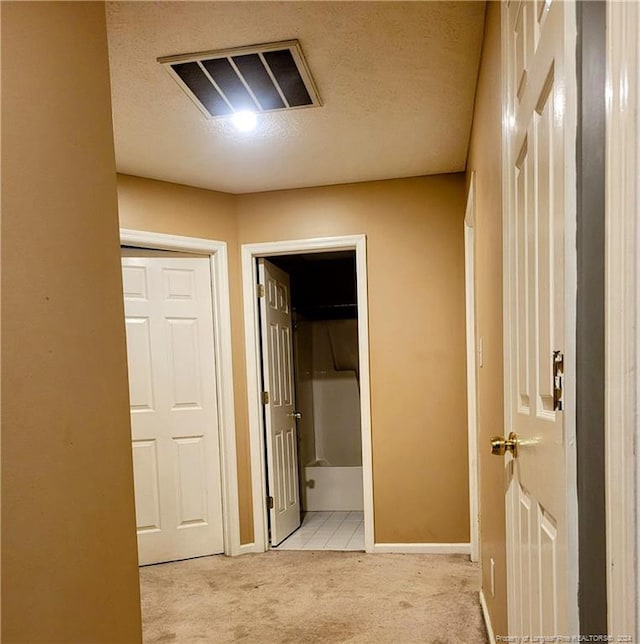 hallway with a textured ceiling and light colored carpet