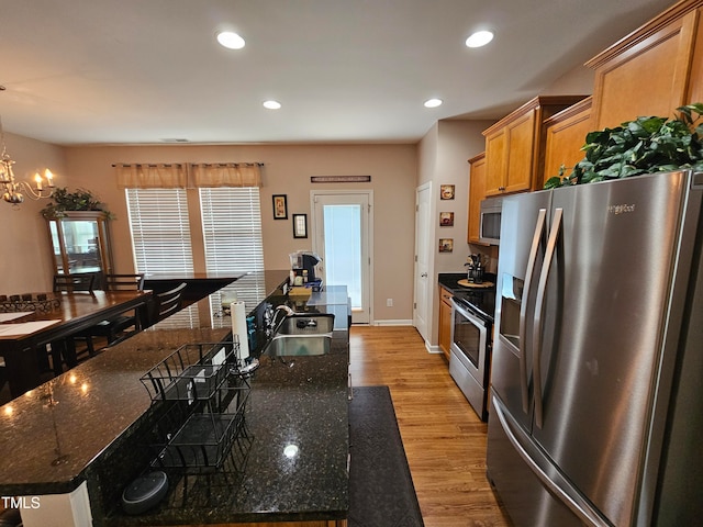 kitchen featuring dark stone countertops, light wood-type flooring, appliances with stainless steel finishes, a chandelier, and sink