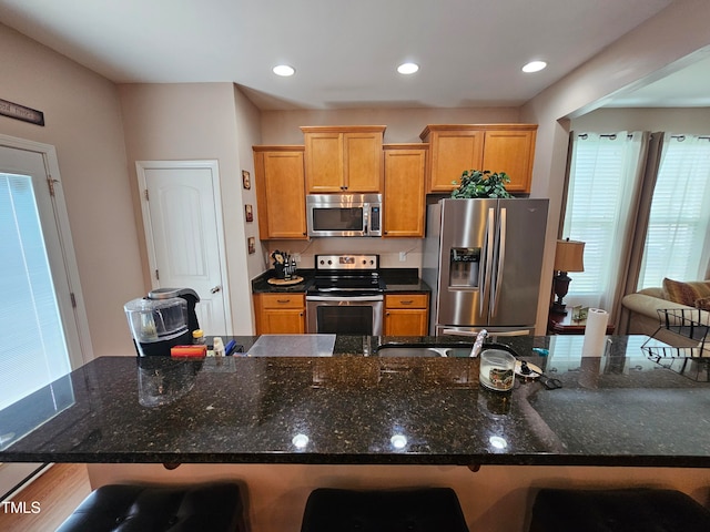 kitchen featuring a spacious island, wood-type flooring, a breakfast bar, stainless steel appliances, and dark stone counters