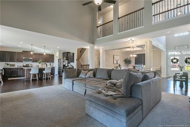 living room with ceiling fan with notable chandelier, dark wood-type flooring, a high ceiling, and decorative columns