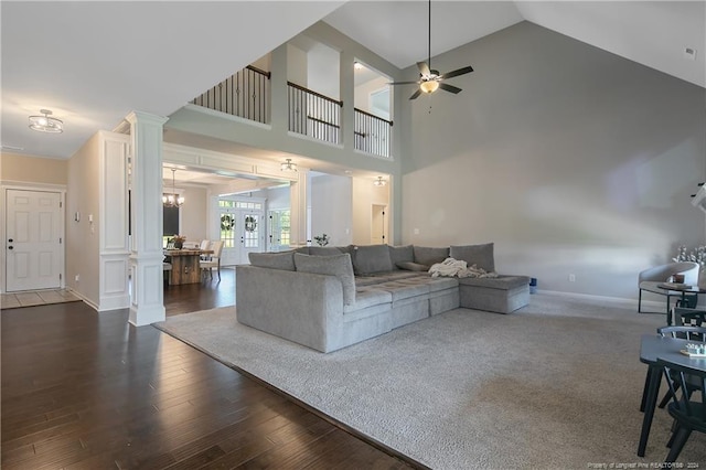 living room featuring ceiling fan with notable chandelier, dark wood-type flooring, high vaulted ceiling, and decorative columns