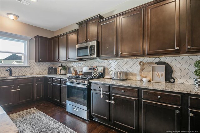 kitchen with dark brown cabinets, backsplash, appliances with stainless steel finishes, dark wood-type flooring, and sink