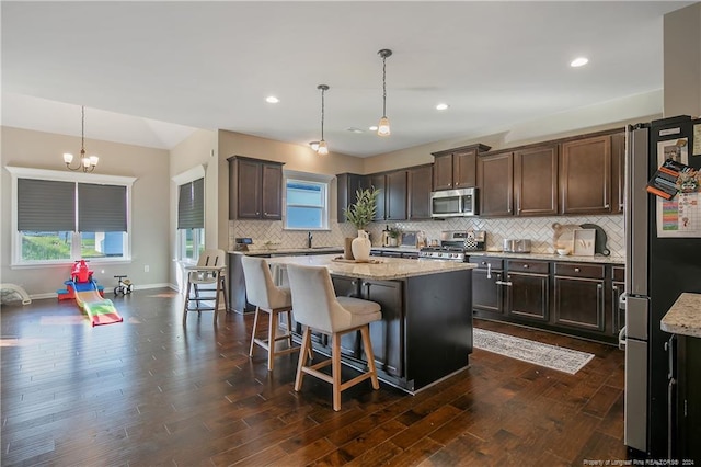 kitchen featuring dark hardwood / wood-style floors, appliances with stainless steel finishes, a center island, and hanging light fixtures