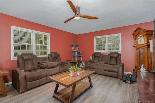 living room featuring ceiling fan, light hardwood / wood-style flooring, and a textured ceiling