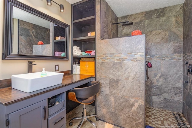 bathroom with vanity, tiled shower, and a textured ceiling