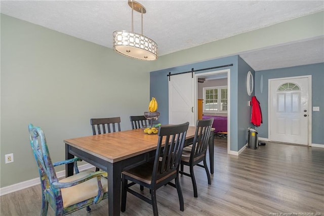 dining area with a barn door, a textured ceiling, baseboards, and wood finished floors