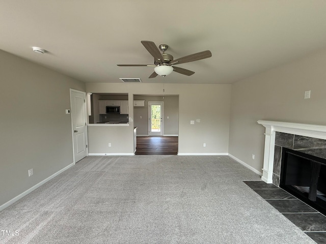 unfurnished living room with a tile fireplace, dark carpet, and ceiling fan