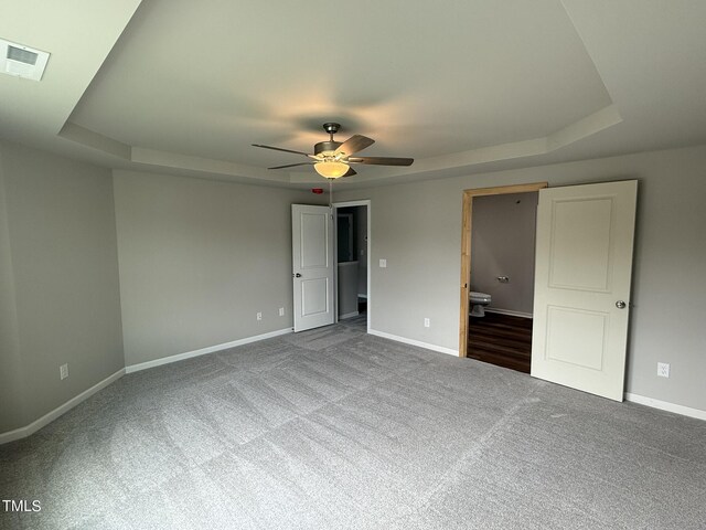 unfurnished bedroom featuring ceiling fan, a raised ceiling, connected bathroom, and carpet flooring