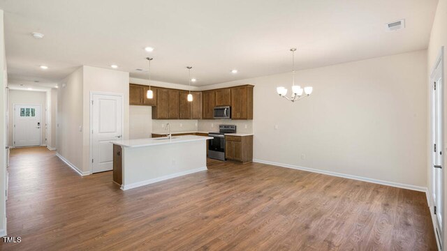 kitchen featuring pendant lighting, appliances with stainless steel finishes, wood-type flooring, and a center island with sink