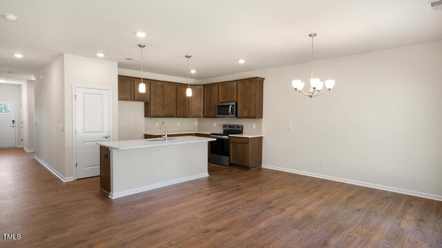 kitchen featuring dark wood-type flooring, decorative light fixtures, a center island with sink, and stainless steel appliances