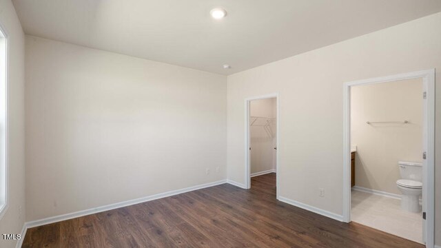 unfurnished bedroom with dark wood-type flooring, ensuite bathroom, a closet, and a walk in closet