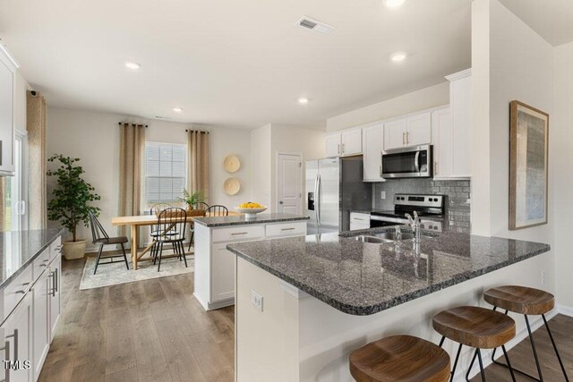 kitchen featuring appliances with stainless steel finishes, white cabinetry, wood-type flooring, and an island with sink