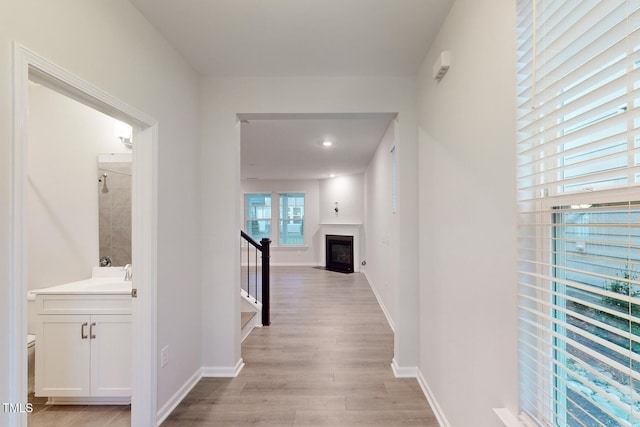 hall featuring light wood finished floors, stairway, baseboards, and a sink