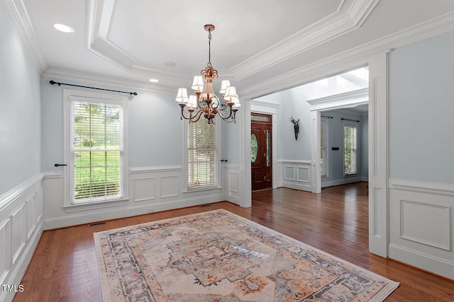 unfurnished dining area with a notable chandelier, a tray ceiling, dark wood-type flooring, and crown molding