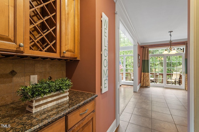 interior space featuring dark stone counters, light tile patterned flooring, hanging light fixtures, backsplash, and crown molding