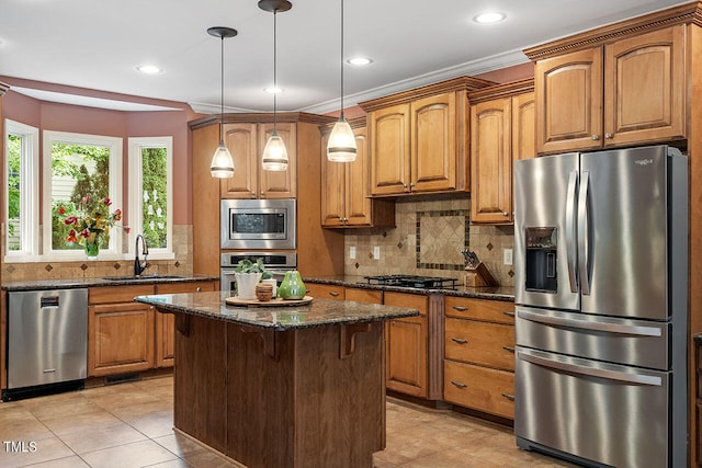 kitchen with pendant lighting, sink, appliances with stainless steel finishes, a center island, and dark stone countertops