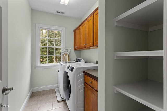 laundry area with separate washer and dryer, light tile patterned floors, and cabinets