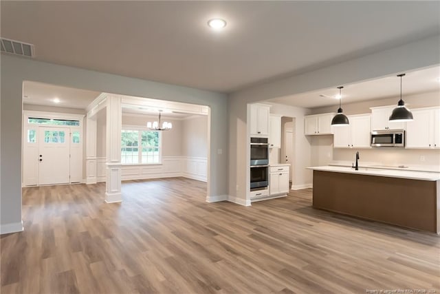 kitchen featuring pendant lighting, white cabinets, stainless steel appliances, and light wood-type flooring