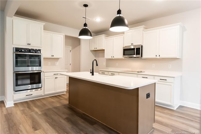 kitchen featuring wood-type flooring, stainless steel appliances, white cabinetry, and an island with sink