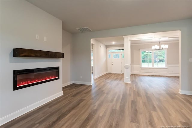 unfurnished living room featuring wood-type flooring, decorative columns, and a notable chandelier