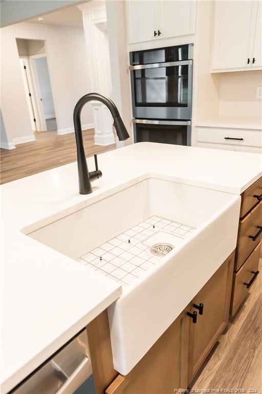 interior details featuring light hardwood / wood-style flooring, white cabinets, stainless steel double oven, and sink