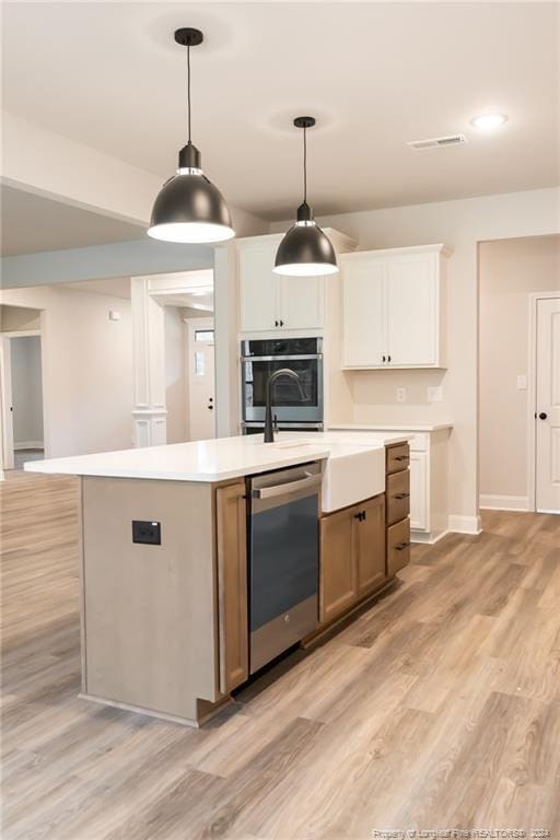 kitchen featuring white cabinets, appliances with stainless steel finishes, a center island with sink, and light hardwood / wood-style floors