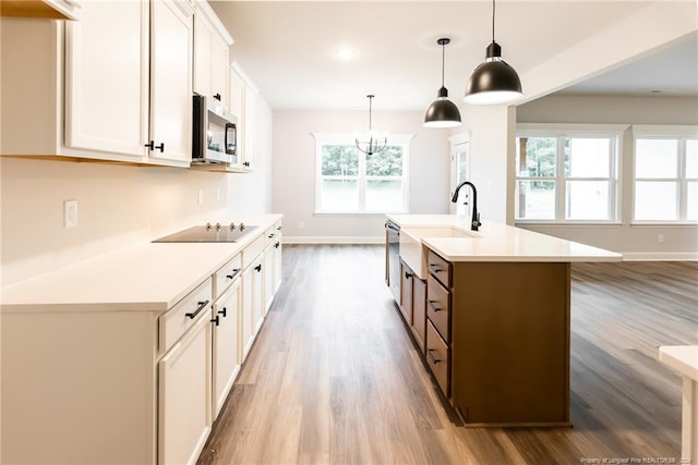 kitchen with hardwood / wood-style floors, pendant lighting, an island with sink, white cabinetry, and stainless steel appliances