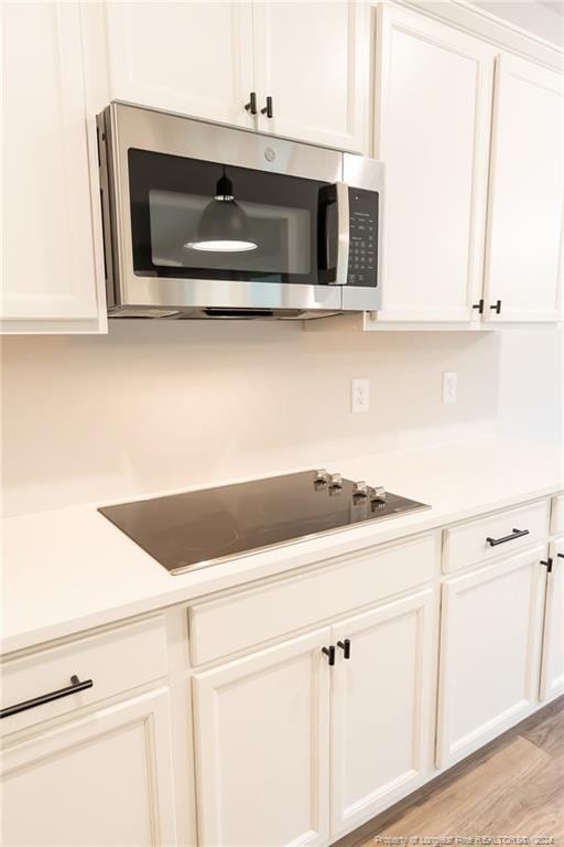 kitchen with black electric stovetop, light hardwood / wood-style floors, and white cabinetry