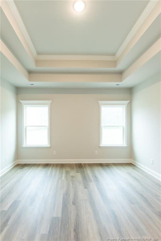 unfurnished room with a raised ceiling, ornamental molding, and light hardwood / wood-style flooring