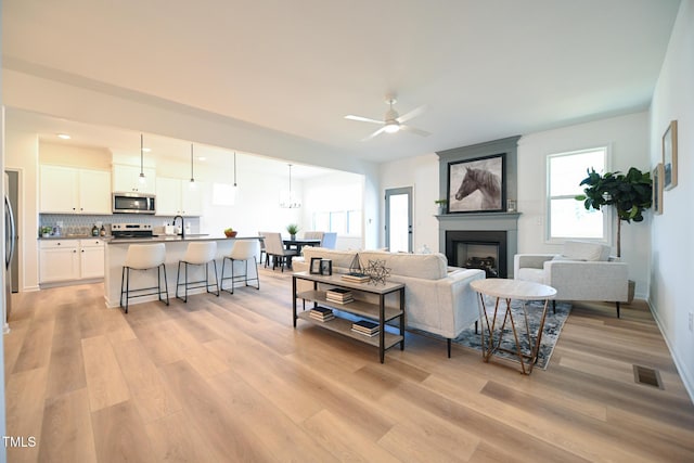 living room with ceiling fan, sink, a fireplace, and light hardwood / wood-style floors