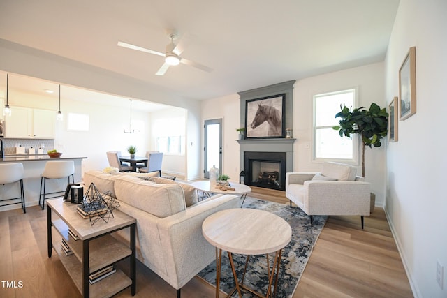 living room featuring a large fireplace, ceiling fan, and light wood-type flooring