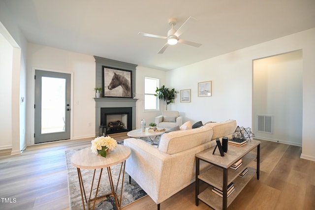 living room with hardwood / wood-style flooring, a large fireplace, and ceiling fan