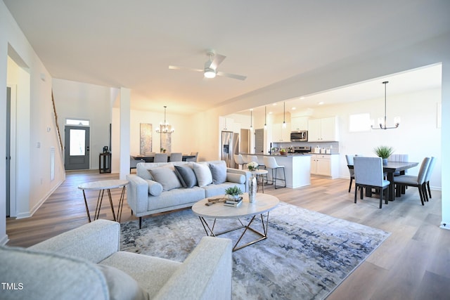 living room with ceiling fan with notable chandelier and light hardwood / wood-style flooring